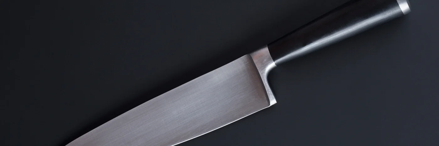 A large sharp kitchen knife lying on a dark surface.
