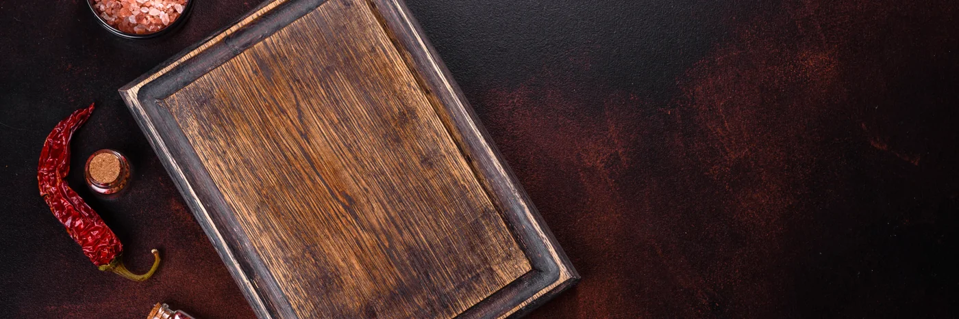 A wooden board with chillies and salt on a dark kitchen surface, seen from above.