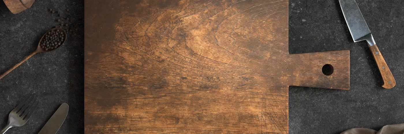 A dark wooden cutting board and a knife on a concrete kitchen counter, seen from above.