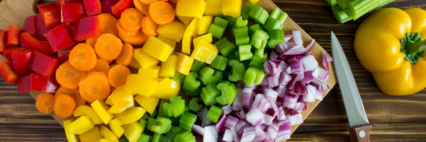 Chopped carrots, peppers, celery and onion arranged on a board, seen from above.