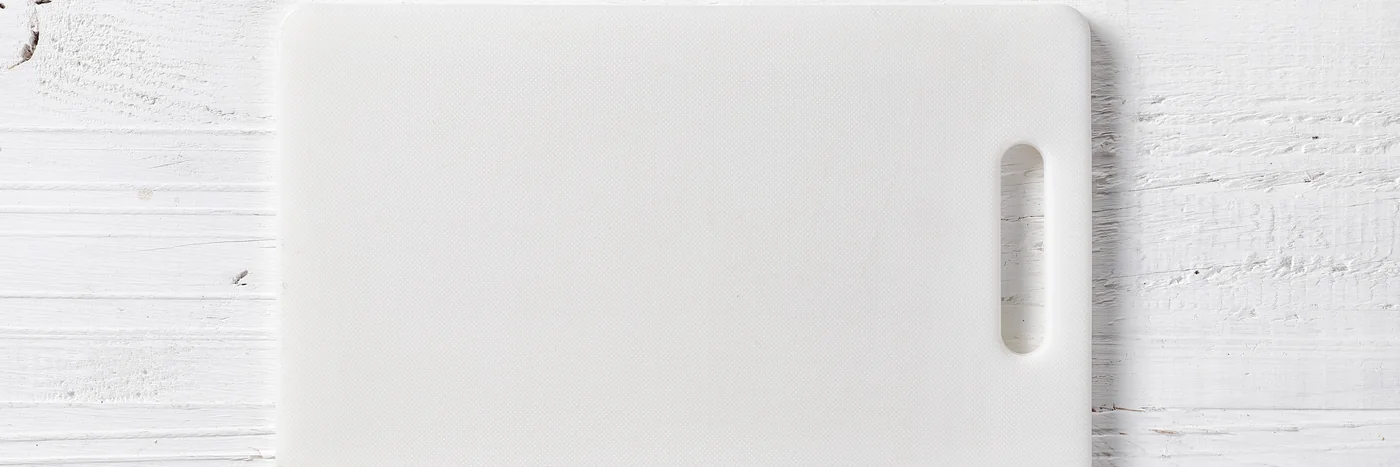 A white plastic cutting board on a pale wooden surface.