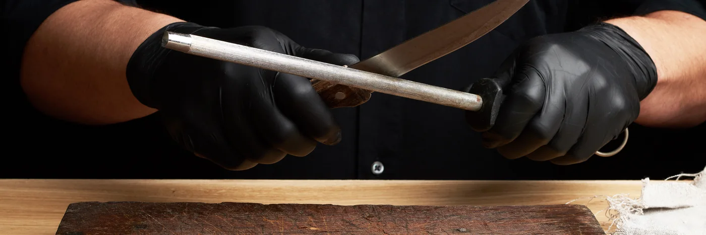 Gloved hands running a kitchen knife along a steel sharpening rod.