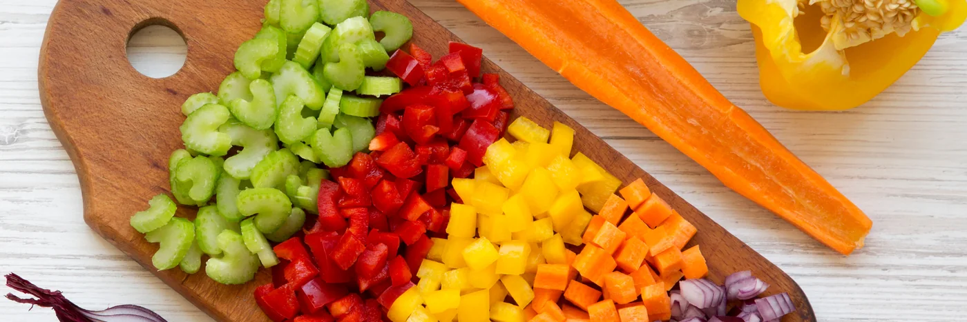 Diced vegetables on a wooden board on a white surface, seen from above.