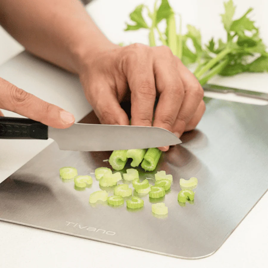 Hands slicing celery on the Vanotium titanium cutting board.